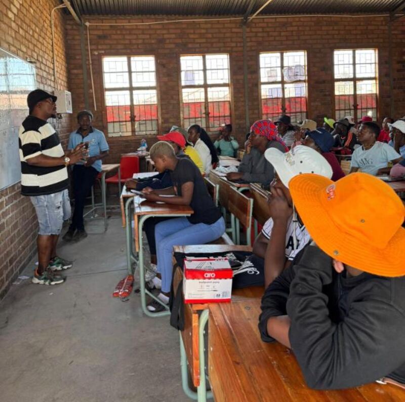 A trainer addressing adult learners seated at desks in a Limpopo classroom during the theoretical training phase.