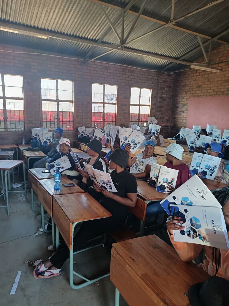 Young learners seated at desks in a Limpopo classroom, holding Kaylord-branded programme brochures.